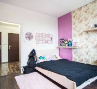 A bedroom in a two-room apartment with floral wallpaper and a wooden decor floor.