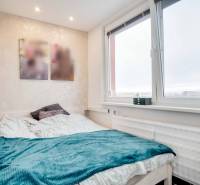 Bedroom in a two-room apartment with a bed, blanket, and large window.
