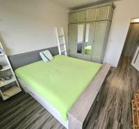 A bedroom in a three-room apartment with a wooden decor floor and a green bed.