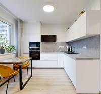 A kitchen in a studio apartment with a window, a dining table, and a floor with a wooden decor.