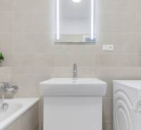 A bathroom with a bathtub, sink, and washing machine in a 3-room apartment, beige ceramic tiles.