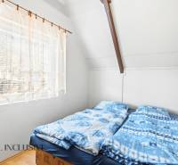 A bedroom in a cottage with an attic, two beds, a window with a curtain, and a floor with a wooden decor.