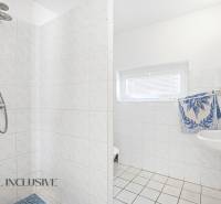 Bathroom in a cabin with tiles, shower, and sink, white walls with a window.