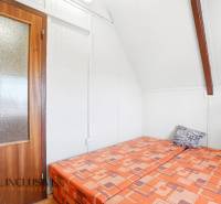 Wooden door, bed with colorful bedding, and white ceiling in the cottage.