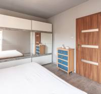 A bright bedroom with a large wardrobe, a mirror, and a wooden dresser in a family house.