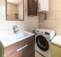 A bathroom in a family house with a washing machine, sink, mirror, and boiler on yellow tiles.