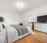 Bright bedroom with a bed, dresser, and television on a wooden floor.