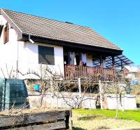 A cottage in Partizánske with a garden and terrace, surrounded by greenery and a blue sky.