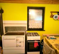 A cottage with a kitchenette, a tiled stove, and a gas stove.