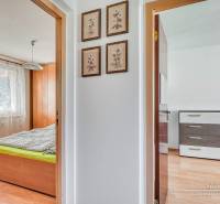 Interior of a 3-room apartment with a wooden decor floor, showing a bedroom and a hallway with paintings.