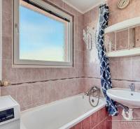 A bathroom in a 3-room apartment with a bathtub, sink, and washing machine, with tiled walls.
