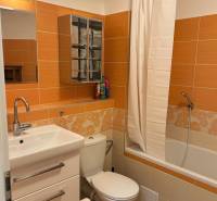 A bathroom with orange and white tiles, a bathtub, a sink, and a toilet in a 3-room apartment.