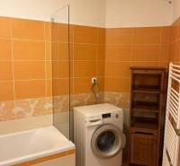 A bathroom in a 3-room apartment with orange tiles, a washing machine, and a bathtub.