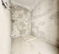 An unfinished wall with plaster and loose cables in a studio apartment.