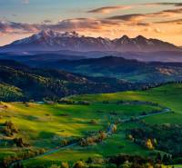A landscape with agricultural and forest land surrounded by mountains in the Hrabkova area at sunset.
