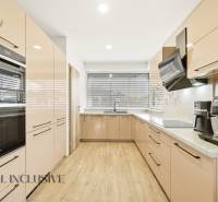 A kitchen in a family house with a wooden decor floor, equipped with appliances and large windows.