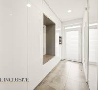 A hallway in a family house with white storage cabinets, tiles, and glass doors.