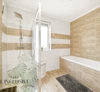 A bathroom in a family house with a bathtub, shower, and tiles with a wooden decor.