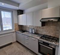 Kitchen area of a 2-room apartment with a gas stove, white cabinets, and a large window.