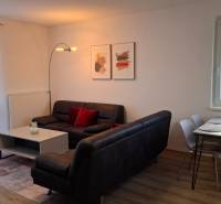Living room in a two-room apartment with a wooden decor floor, a sofa, and a dining table.