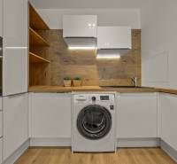 A kitchen with white cabinets, a sink, a washing machine, and wooden decor in a 2-room apartment.