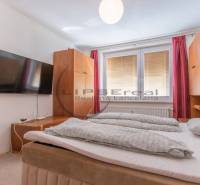 A one-bedroom apartment with a large bed, a wall-mounted TV, and red curtains.