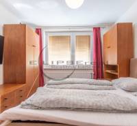 A bedroom in a studio apartment with a bed and wooden furniture, a TV on the wall.