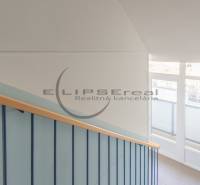 A staircase with a wooden railing and a large window illuminating the space on Štúrova Street in Malacky.
