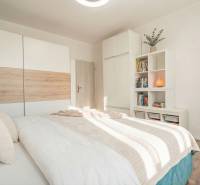 A bright bedroom with a bed, wardrobe, and shelf in a 2-room apartment with a wooden decor floor.