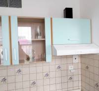 A kitchen with pastel cabinets, tiles, and a range hood in a studio apartment.