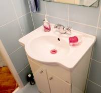 A bathroom with a sink, a glass shelf, and light blue tiles in a studio apartment.