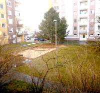 A courtyard surrounded by apartment buildings and trees in Piešťany, an ideal space for a 1-bedroom apartment.