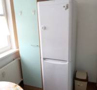 A refrigerator and a cabinet in the kitchen of a one-room apartment with a ceramic floor.