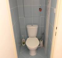 A bathroom in a one-room apartment with light blue tiles and a white toilet.