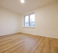 An empty room in a family house with a wood-patterned floor and a large window.