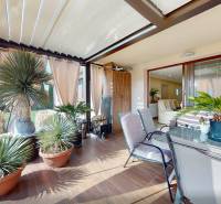 Covered terrace of a family house with plants and seating, floor with wooden decor.