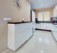 A kitchen in a family house with glossy cabinets and light ceramic flooring.