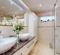 A family house bathroom with two sinks, a shower corner, and decorative flowers.