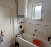 A bathroom in a family house with a bathtub, electric boiler, window, and floor with wooden decor.