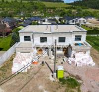 A family house under construction in Harichovce, surrounded by greenery and other houses.