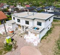 Construction of a family house in Harichovce with building materials and neighboring houses in the background.