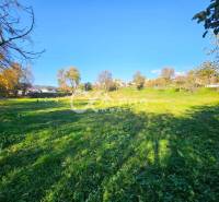 A vast green plot in Spišské Podhradie designated for housing, surrounded by trees and houses.