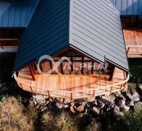 A family house in Hnilčík with a wooden terrace and a sloped roof among natural elements.
