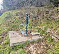 A manual pump on a concrete base next to a stone wall in Helcmanovce.