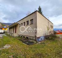 A building in Helcmanovce with grassy surroundings and neighboring houses, surrounded by hills.