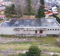 A building in Helcmanovce with a sloped roof, surrounded by greenery and other structures.