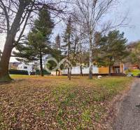 A building in Helcmanovce surrounded by trees, along an asphalt road, with autumn leaves.