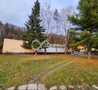 A building in Helcmanovce surrounded by trees, with a neighboring road and vehicles.