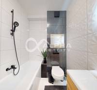 A bathroom in a 2-room apartment with a bathtub, toilet, and plant, highlighted by white tiles.