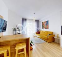 Living room in a two-room apartment with a wood-patterned floor, yellow sofa, and television.